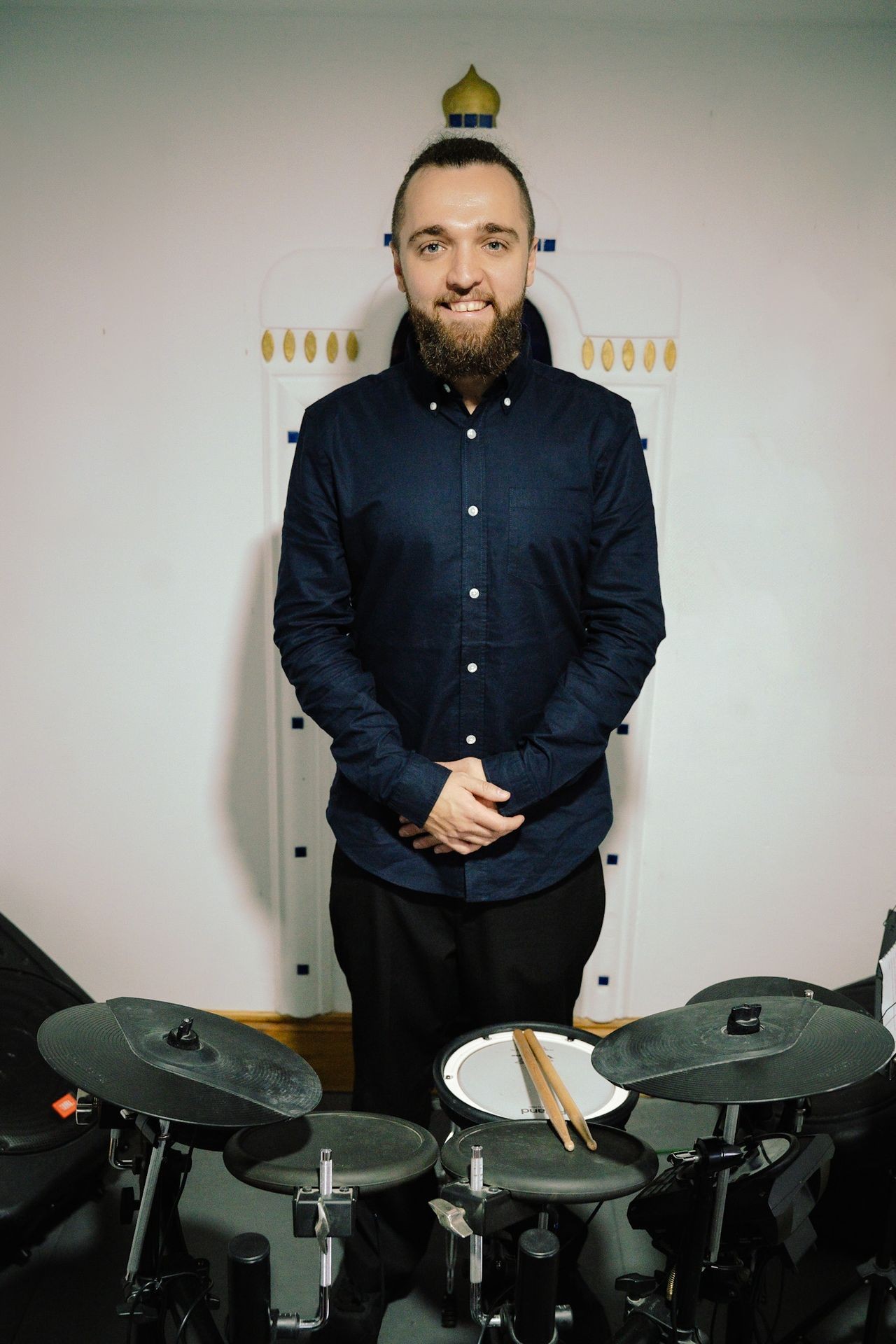 Person standing behind an electronic drum kit with drumsticks placed on the snare drum.