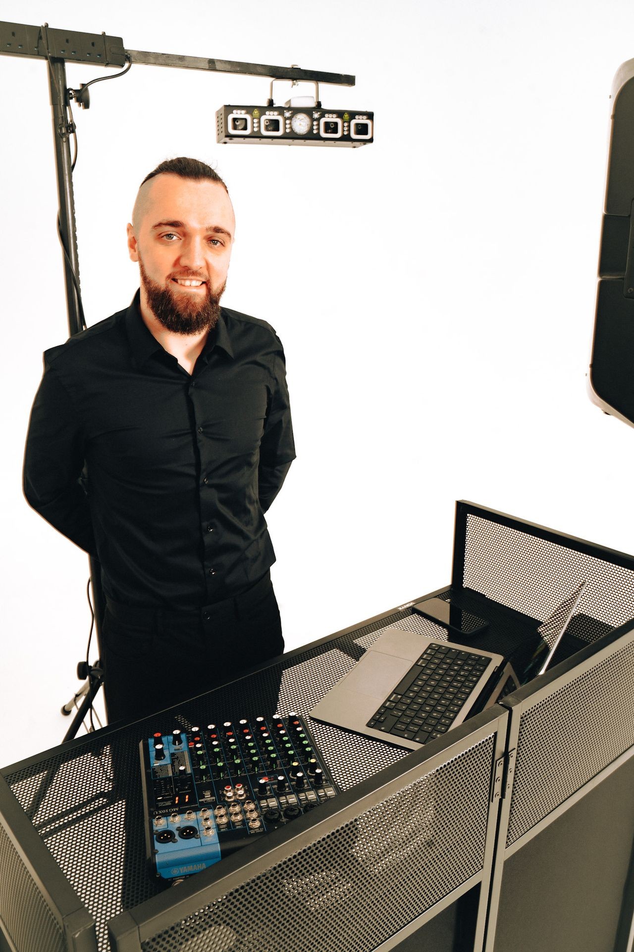 Man in black shirt standing behind a DJ setup with mixer and laptop.