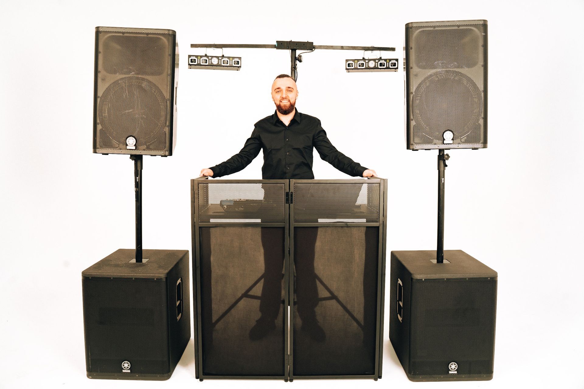 Person standing behind a DJ booth with large speakers and lighting equipment on both sides.