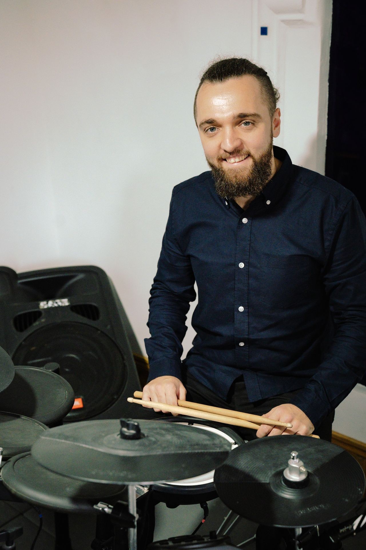 Person with a beard holding drumsticks, seated at an electronic drum set.